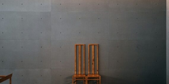 Two warm wooden chairs against a cool gray concrete wall